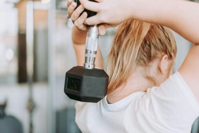 woman holding dumbbell in white crew-neck t-shirt