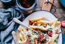 “밤마다 허기가 지고 잠을 설쳐요”… 야식 유혹, 진짜 배고픔일까? bacon strips and melted cheese topped fries on oval white and blue platter with gray stainless steel forks