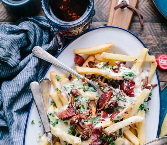 “밤마다 허기가 지고 잠을 설쳐요”… 야식 유혹, 진짜 배고픔일까? bacon strips and melted cheese topped fries on oval white and blue platter with gray stainless steel forks