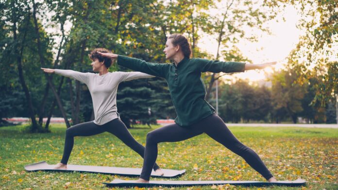 Photo by Vitaly Gariev Two women practicing yoga warrior pose outdoors.