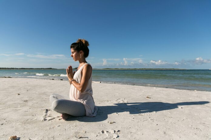 Photo by Amelia Bartlett woman praying and sitting on sand seashore during day